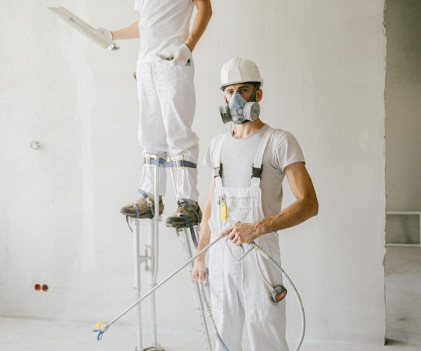 Two painters in protective gear working on a home renovation project, wearing masks and white uniforms.